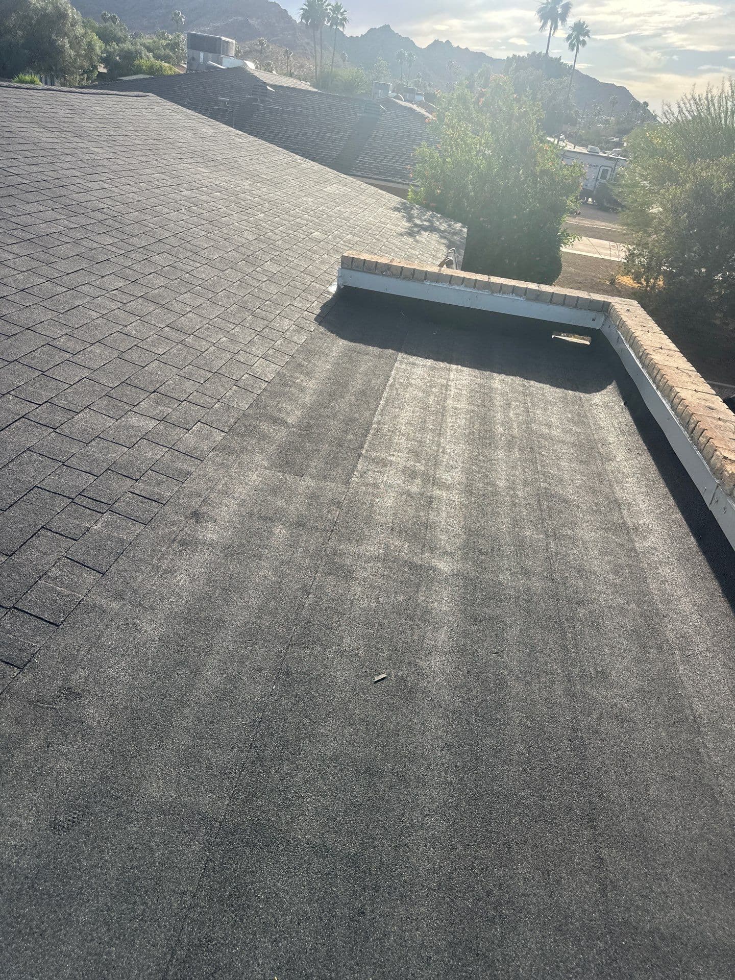 Roof view showcasing black shingles and a flat roofing section under a sunny sky.