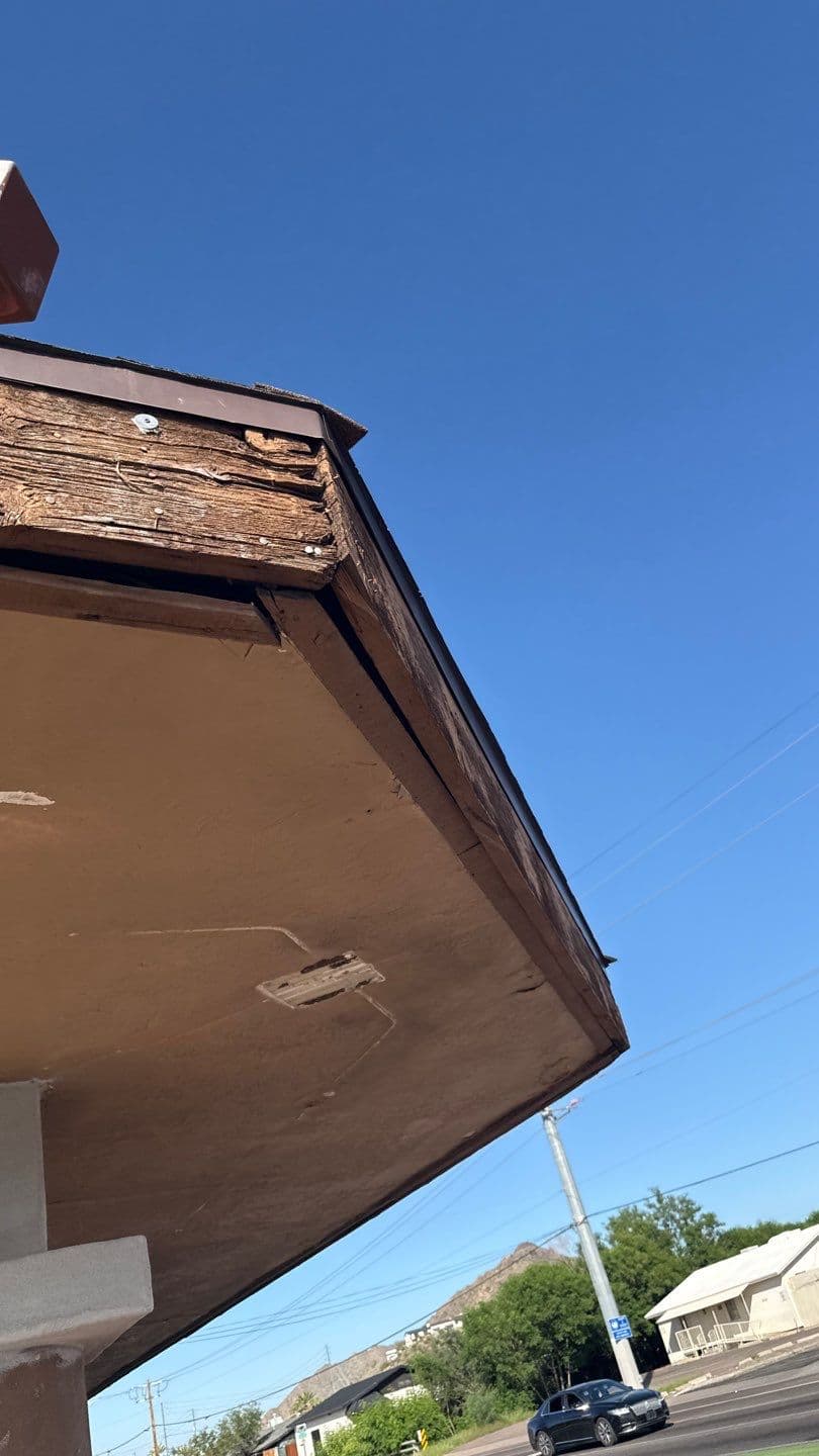 Weathered building eaves showing wood damage against a clear blue sky.